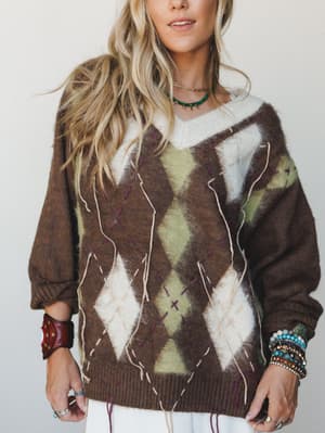 An oversized argyle sweater in mocha, cream, and sage styled with layered bracelets and a turquoise choker — the kind of sweater that makes you look like you've been thrifting for decades in the best possible way.