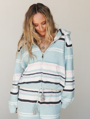 A cozy striped hoodie-and-pants set in soft sky blue, white, navy, and blush — worn with a layered pendant necklace and that 'just woke up feeling good' energy.