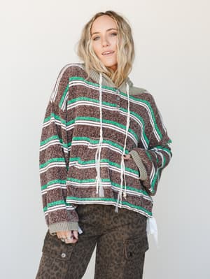A relaxed striped hoodie in chocolate brown, emerald green, and cream is layered over an olive knit hoodie, paired with leopard print cargo pants — the kind of effortless, textured layering that looks like it took zero effort and exactly the right am