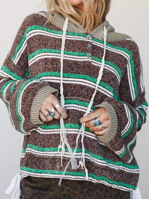 A cozy striped knit hoodie in chocolate brown, kelly green, and cream gets the boho treatment with braided drawstrings, bead-tipped tassels, and stacked silver and turquoise rings — the kind of sweater you reach for every single weekend.