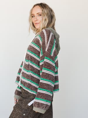 A boucle-textured striped hoodie in chocolate brown, white, and bright green is styled with leopard print cargo pants — casual and a little unexpected, in the best way.