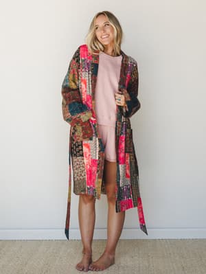 A patchwork duster coat layered over a dusty pink sweatshirt and shorts set — the kind of outfit that makes staying home feel like a whole personality.