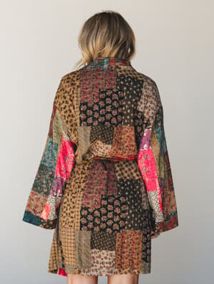Shot from behind, a model wears a stunning patchwork kimono jacket in a rich mix of earthy tones and bold pops of pink — the kind of piece that looks like it was stitched together from a lifetime of beautiful fabric finds.