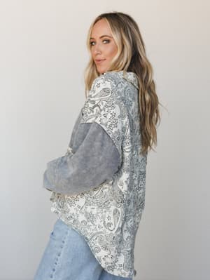 Shot from a three-quarter back angle, this oversized mixed-print jacket layers a cream and grey paisley body against contrasting grey houndstooth sleeves — worn over light wash jeans with that effortless, 'grabbed it on the way out' energy.