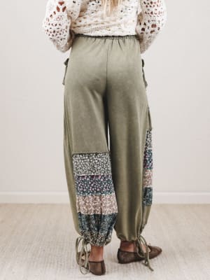 Person wearing olive green pants with floral patchwork details on a plain background