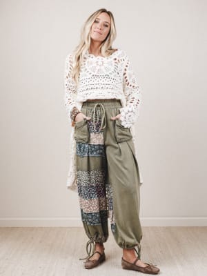 Woman wearing a white crochet top and patterned pants with a neutral background