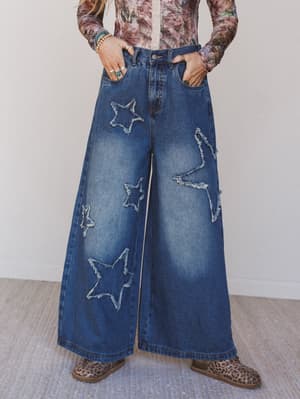 Person wearing blue jeans with star designs and a patterned top on a neutral background