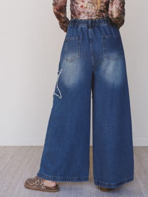 Person wearing wide-leg blue jeans with a plain background