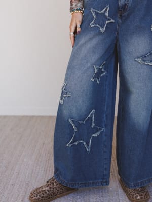 Blue jeans with star patches worn by a person on a neutral background