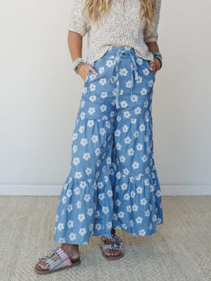 A breezy, retro-leaning wide-leg pant in chambray blue with bold daisy print, styled with a multicolor speckle knit top and embellished sandals — the kind of outfit that looks intentional without trying.