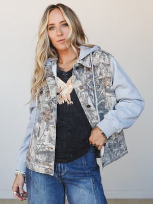 A laid-back, effortlessly cool look built around a mixed-media hooded jacket — camo-print denim body with heathered grey sweatshirt sleeves — layered over a washed black eagle graphic tee and relaxed dark wash jeans.