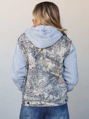 A back-view shot of a hybrid denim jacket layered over a heathered blue hoodie, the camo-style leaf print body contrasting softly against the cozy sweatshirt sleeves — effortlessly relaxed and a little unexpected.