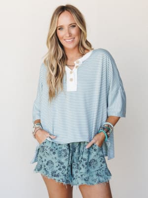 A breezy, easygoing outfit pairing an oversized blue-and-white striped henley top with floral ruffle shorts — the kind of look that feels like summer weekends with zero effort required.