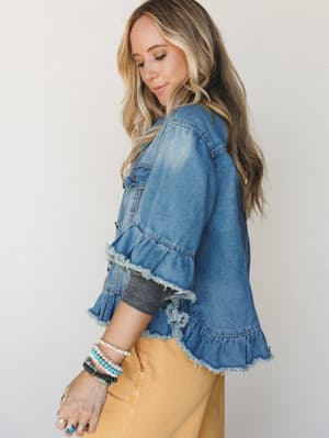 A denim jacket with unexpected personality — ruffle and raw-edge hem details give this classic silhouette a boho twist, styled with golden mustard bottoms and a stack of turquoise and pearl bracelets for that effortlessly collected look.