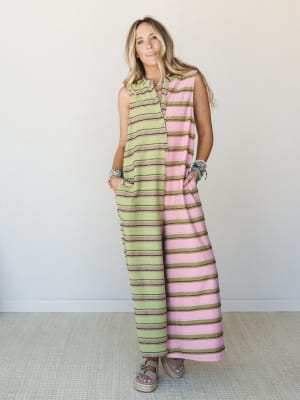 A full-length striped jumpsuit in a playful color-block of lime green and dusty pink with olive and brown stripe details, styled with stacked turquoise bracelets and platform sandals against a clean studio backdrop.