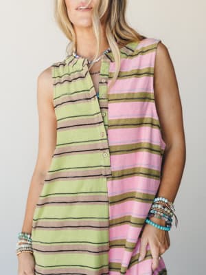 A sleeveless color-blocked striped jumpsuit styled with stacks of beaded bracelets and a layered necklace — two different stripe colorways sewn together for a playful, collected feel.