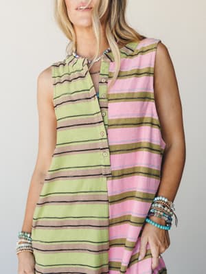 A sleeveless color-blocked striped jumpsuit styled with stacks of beaded bracelets and a layered necklace — two different stripe colorways sewn together for a playful, collected feel.