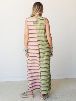 A color-blocked striped maxi jumpsuit shot from the back — pink on one side, olive green on the other — styled with stacked turquoise bracelets and platform espadrilles for an easy, expressive warm-weather look.