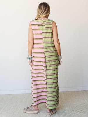 A color-blocked striped maxi jumpsuit shot from the back — pink on one side, olive green on the other — styled with stacked turquoise bracelets and platform espadrilles for an easy, expressive warm-weather look.