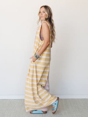 A breezy striped maxi jumpsuit in soft mustard and blush worn with turquoise buckle sandals and a stack of beaded bracelets — the kind of outfit that looks equally at home on a boardwalk or a back patio.
