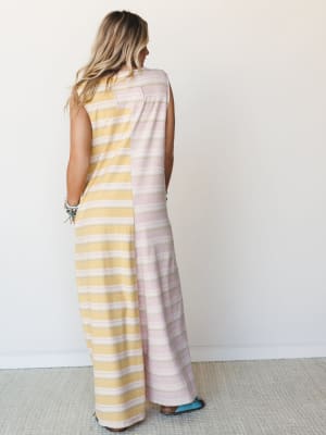 A back-facing shot of a maxi jumpsuit in a color-blocked stripe design — one side butter yellow, the other dusty rose — with a relaxed, wide-leg silhouette that feels effortlessly warm-weather ready, styled with stacked turquoise bracelets and wester