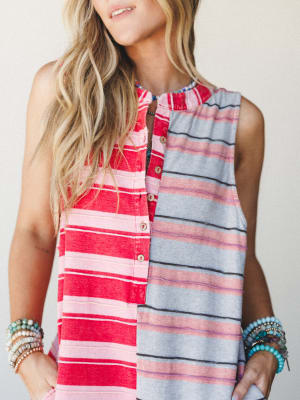A close-up torso shot of a color-blocked striped sleeveless jumpsuit in red and grey, styled with stacks of beaded bracelets — easy, expressive, and ready for wherever the day takes you.