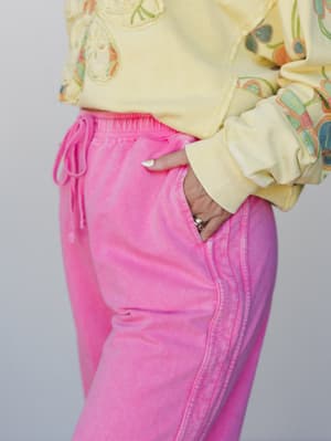 A close-up mid-shot of acid-washed pink wide-leg sweatpants styled with a butter yellow floral embroidered cropped sweatshirt — the kind of outfit that feels like a good mood made wearable.