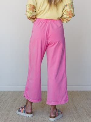 A back-view shot of wide-leg cropped pink pants paired with a yellow floral-embroidered sweatshirt and colorful woven platform sandals — casual, playful, and very much the outfit you'd wear when you want to be comfortable AND the most fun person in t