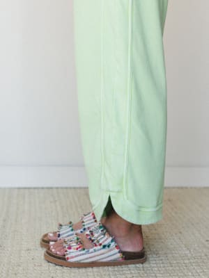 A close-up of cropped wide-leg pants in a soft mint green, paired with colorful fringe-trimmed slide sandals on a jute rug — the kind of effortless combo that makes a Tuesday feel intentional.