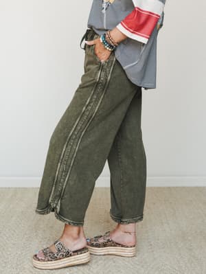 A side-profile shot showing olive mineral-wash wide-leg crop pants styled with a striped colorblock top, stacked bead bracelets, and leopard print platform sandals — relaxed and expressive in the best way.