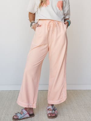Soft peach wide-leg pants with a drawstring waist styled with a seashell graphic tee, beaded sandals, and stacked bracelets — the kind of easy, feel-good outfit that works just as well for a beach town stroll as it does for doing absolutely nothing.