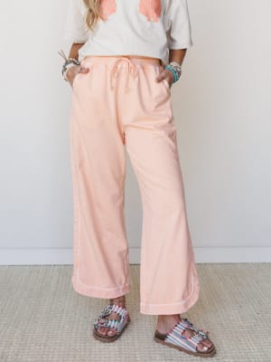 Soft peach wide-leg pants with a drawstring waist styled with a shell-print graphic tee, beaded bracelets, and colorful embellished sandals — relaxed, sun-warmed, and effortlessly put-together.