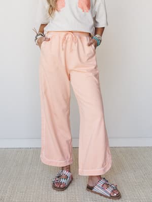Soft peach wide-leg pants with a drawstring waist styled with a shell-print graphic tee, beaded bracelets, and colorful embellished sandals — relaxed, sun-warmed, and effortlessly put-together.
