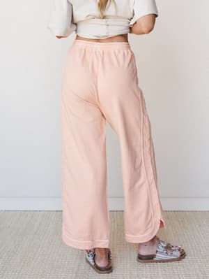 Soft peach wide-leg pants with contrast stitching and a banded hem are styled with a cream crop top and beaded sandals — the kind of easy, put-together look that works just as hard on a coffee run as it does on the couch.