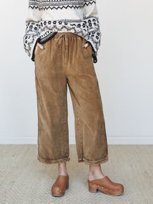 A cozy fall outfit pairing wide-leg washed brown corduroy pants with a fair isle sweater tucked loosely at the waist, grounded by tan studded platform clogs — the kind of outfit that looks like it came together effortlessly but absolutely did not.
