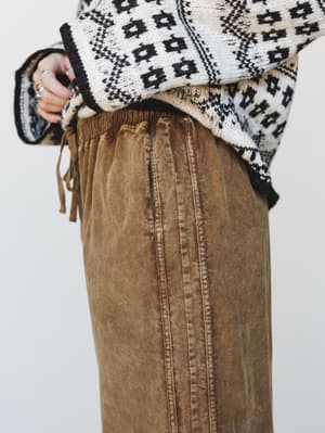 A close-up detail shot of wide-leg corduroy pants in a warm washed brown, paired with a cream and black Fair Isle knit sweater — the kind of outfit that makes Saturday feel intentional.