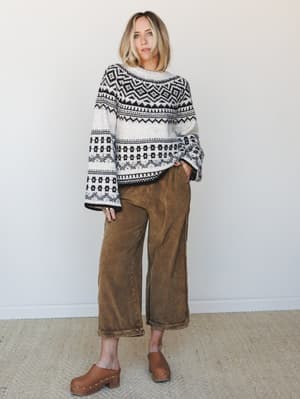 A relaxed full-body shot of a model in a Fair Isle sweater with wide bell sleeves paired with washed brown wide-leg corduroy pants and studded wood clogs — the kind of outfit that looks effortless but clearly took two seconds of good instinct.
