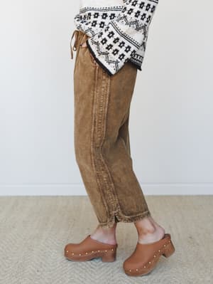 A side-angle shot of relaxed, washed brown wide-leg pants styled with a fair isle sweater and tan studded clogs — the kind of effortless fall outfit that looks like you tried just enough.