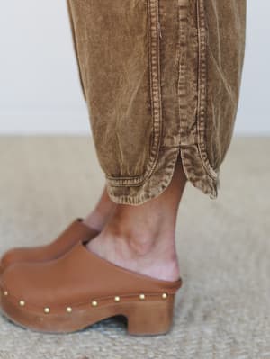 A close-up detail shot of washed brown corduroy pants with a gathered ankle hem, paired with tan leather platform clogs with gold stud trim — earthy, relaxed, and very much the kind of outfit you'd wear to a farmers market without overthinking it.