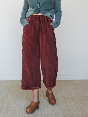 Wide-leg cropped corduroy pants in a rich washed burgundy, styled with a knotted teal thermal and brown studded clogs — the kind of put-together-but-comfortable outfit that makes Saturday errands feel intentional.