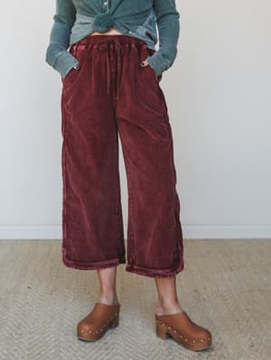 Wide-leg cropped corduroy pants in a washed burgundy paired with a knotted teal thermal and brown studded clogs — the kind of outfit that looks effortless but was absolutely thought through.