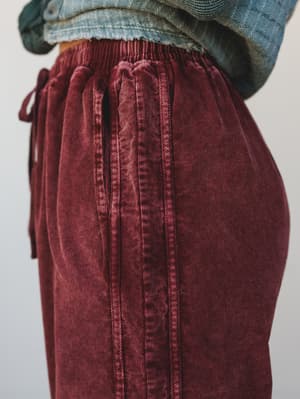 A close-up detail shot of wide-leg corduroy pants in a rich washed burgundy, layered under a cropped denim top — the texture and drawstring waist doing all the talking.