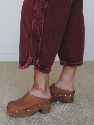 A close-up detail shot of cropped wide-leg corduroy pants in washed burgundy, paired with tan leather platform clogs with gold stud trim — earthy, intentional, and very much the kind of outfit that makes you feel put-together without trying too hard.