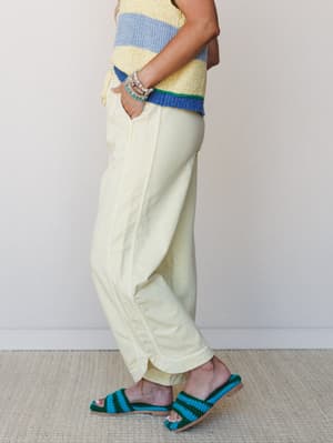 A side-profile shot of a model in butter yellow wide-leg pants paired with a color-blocked striped knit top and crochet slide sandals — the whole look has that easy, sunny energy of a good Saturday with nowhere to be.