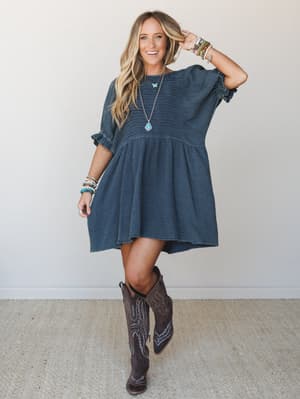 A breezy gauze mini dress in deep navy styled with tall western boots and layered turquoise jewelry — casual and free-spirited with just enough boho-country crossover to feel totally effortless.