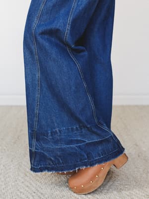A close-up detail shot of wide-leg dark wash denim hitting the floor in a sweep of indigo, paired with tan studded clogs — very much the '70s-library-girl energy we're here for.