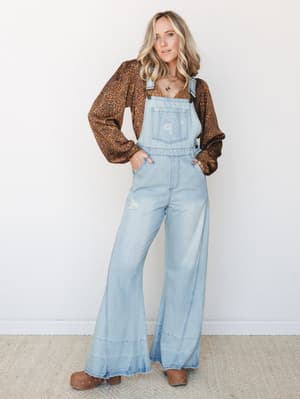 Wide-leg denim overalls styled over a leopard print long-sleeve top with clogs and layered necklaces — that effortless 70s-meets-weekend energy that makes you want to immediately get dressed.