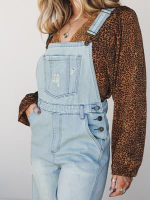 Light wash denim overalls styled over a rust leopard print long-sleeve top with lace trim peeking at the neckline — the kind of effortless layering that looks like it took no effort but absolutely did.