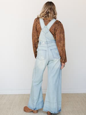 Shot from the back, she's wearing wide-leg light wash denim overalls over a leopard print long-sleeve top — the kind of effortless layering that looks like it came together without trying.