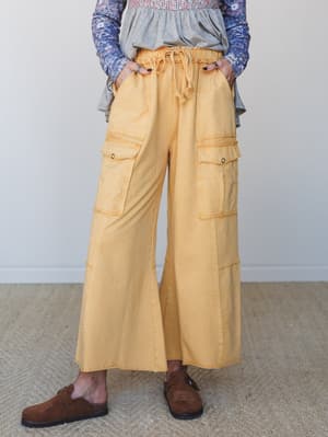 Wide-leg cargo pants in a faded mustard yellow styled with a layered floral top and brown suede clogs — relaxed and intentional, like she got dressed on purpose but made it look effortless.